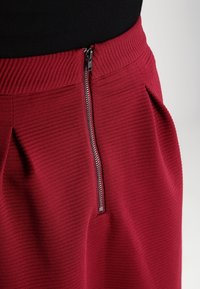 Gonna in tessuto rigato rosso con chiusura a zip metallica visibile in vita, caratterizzata da pieghe per maggiore texture e forma.