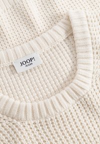 Collo di maglione lavorato a maglia color crema con bordo a coste e etichetta bianca del marchio JOOP! JEANS cucita all'interno.