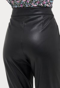 Calças de couro pretas de cintura alta com uma textura suave, com costuras frontais e um silhueta ajustada, combinadas com uma blusa de padrão floral.
