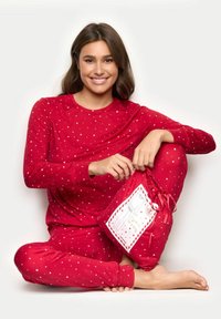 Czerwony zestaw pidżamowy z długim rękawem w białe gwiazdki. Miękka tkanina, z dopasowanymi mankietami. Zawiera dopasowaną torbę prezentową z ozdobną etykietą.