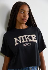 Zwarte cropped T-shirt van katoen, met gedurfde "NIKE" logo in crème en paars, korte mouwen en een ontspannen pasvorm.