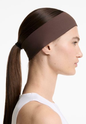 Bruine stoffen haarband gedragen met steil, lang haar in een staart, zijaanzicht tegen een lichte achtergrond.