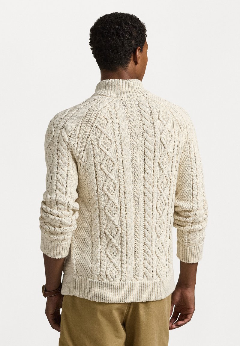 Maglione a maglia cable color crema con collo alto, caratterizzato da motivi a rombo e coste, e maniche testurizzate. Vestibilità casual con orlo a coste.