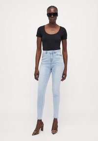Bodysuit negro de manga corta, jeans de tiro alto en azul claro y zapatos de tacón con estampado animal. Las gafas de sol completan el conjunto.