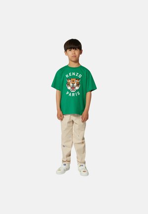 Groene katoenen t-shirt met een tijgerafbeelding en "KENZO PARIS" tekst, gecombineerd met lichtgestreepte broek en witte sneakers met kleurrijke accenten.