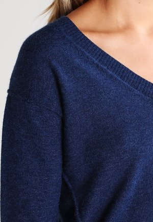 Pull en maille bleu marine avec un décolleté en V, texture douce et col côtelé. Caractéristiques des manches amples et une coupe légèrement décontractée.