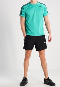 Turquoise athletic t-shirt with black shoulder stripes, paired with black shorts and black sneakers, featuring the Adidas logo on the shirt.