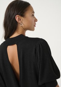 Top en maille noire avec une finition texturée, présentant une découpe au dos et des manches bouffantes. Design simple et élégant avec un col rond.