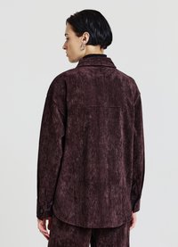 Camicia bordeaux con texture, maniche lunghe, colletto e polsini con bottoni. Presenta una vestibilità comoda e un dettaglio con cucitura sul giogo posteriore.