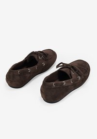 Zapatos de ante marrón con punta redondeada, cordones frontales y ojetes plateados. El diseño presenta un perfil bajo y una parte superior texturizada.