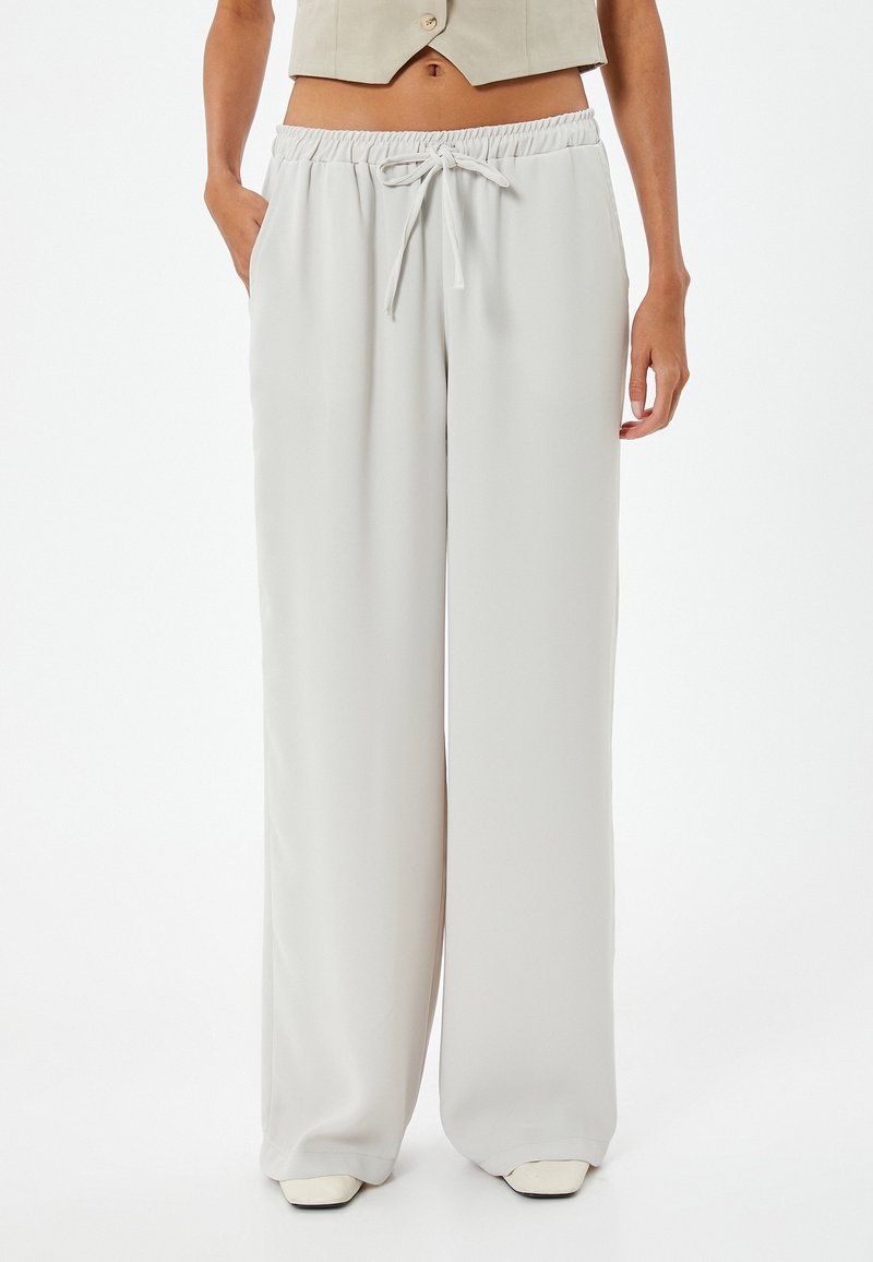 Pantalon large gris clair en tissu lisse, avec une taille élastique et un cordon de serrage, ainsi que des poches latérales.
