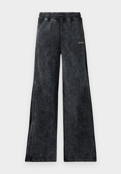 Weite Hosen aus einem strukturierten schwarzen Stoff mit einem subtilen Glanz. Mit einem elastischen Bund und einem kleinen grünen Logoakzent auf der Vorderseite.