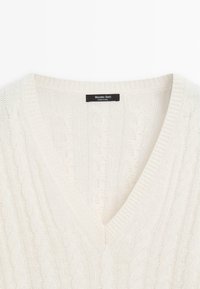 Maglione lavorato a maglia color crema con scollo a V, caratterizzato da un motivo a treccia e dettagli a costine lungo i bordi. Etichetta visibile all'interno.