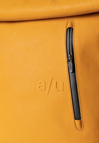 Borsa a rotolo gialla con tasca laterale con zip, logo in rilievo "a/u", texture liscia e hardware della cerniera nera a contrasto.