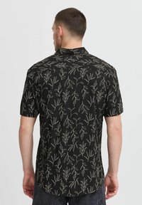Chemise à manches courtes en tissu noir avec des motifs de feuilles blanches, présentant un ourlet droit et un col classique, légère avec une texture lisse.