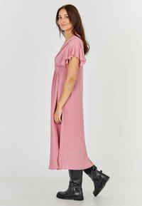 Vaaleanpunainen polvipituinen mekko, jossa on lyhyet röyhelösateet, gathered vyötärö ja pehmeä, virtaava pinta. Yhdistetty mustiin nilkkabootseihin.