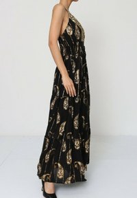Robe maxi noire avec des motifs paisley dorés, présentant un design à col halter et un ourlet froncé. Confectionnée dans un tissu léger avec une texture fluide.