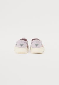Világos lila slip-on cipők, texturált felsőrésszel, krémszínű talppal, és két háromszög alakú logóval a sarokrészen. Narancssárga kiegészítők.