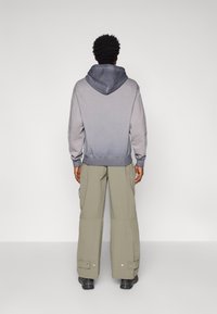 Sweatshirt cinza com capuz e um design em gradiente, combinado com calças cargo largas em verde-azeitona, com bolsos laterais e fechos de botão.