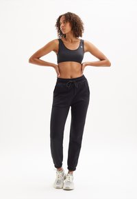 Zwarte sportieve crop top met geribbelde halslijn, gecombineerd met zwarte joggers met een elastische tailleband en boorden, aangevuld met grijze sneakers.