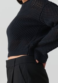 Strickpullover in Marineblau mit strukturiertem, offenem Strickmuster, rundem Ausschnitt und gerippten Bündchen. Kombiniert mit hochgeschnittenen schwarzen Hosen.