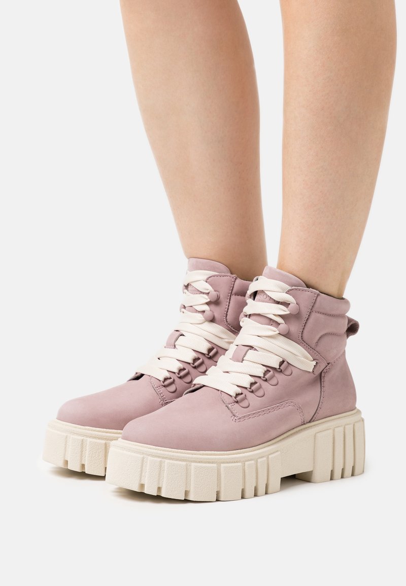 Botas de tobillo de cuero rosa con cordones blancos y una suela gruesa beige, con un acabado texturizado y ojales redondos para el cordón.