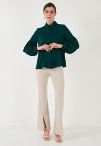 Green blouse with puffed sleeves and button details, paired with beige flared pants featuring slits at the hem. Heels complete the outfit.