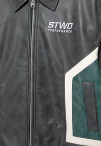 Giacca in pelle nera con chiusura a zip, caratterizzata da accenti bianchi e verdi, tessuto texturizzato e logo ricamato "STWD PERFORMANCE".