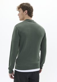 Temno zelena dolga majica z dolgimi rokavi iz mehkega materiala, z rebrastim robom in manšetami, klasično ovratnico in preprostim dizajnom.