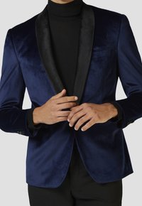 Námorně modrý sametový blazers s černým saténovým šálovým límcem, jednou kapsou a knoflíkovými manžetami, nošený přes černý rolák.