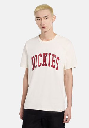 T-shirt di cotone color crema con un logo rosso "DICKIES" curvato sul petto, colletto rotondo e maniche corte.