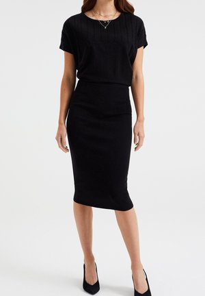 Zwarte geribbelde jurk met een gestructureerde top met korte mouwen en een aansluitende midi-rok. Gecombineerd met zwarte hoge hakken.