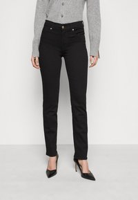 Jeans negros ajustados con una textura suave, con cierre de botón y bolsillos frontales, combinados con tacones negros de punta. 