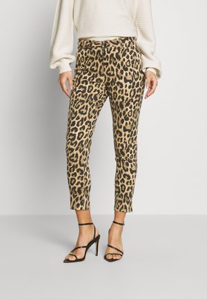 Vrouw draagt beige en zwart, slank aangesloten broek met luipaardprint, een witte geribbelde longsleeve en zwarte sandaaltjes met hoge hakken en bandjes.