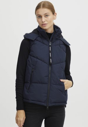 Gilet rembourré bleu marine avec un zip à l'avant, capuche amovible et deux poches latérales. Comprend des sections matelassées et des tirettes de fermeture éclair avec logo.