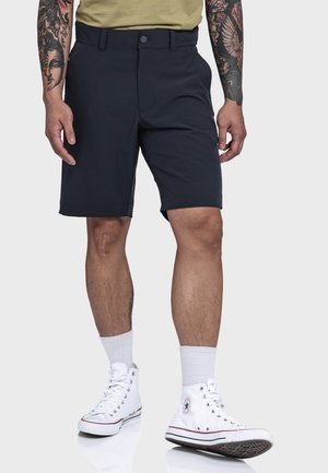 Marineblau Shorts aus leichtem Material, mit flachem Frontdesign, seitlichen Taschen und umgeschlagenem Saum, kombiniert mit weißen High-Top Turnschuhen.