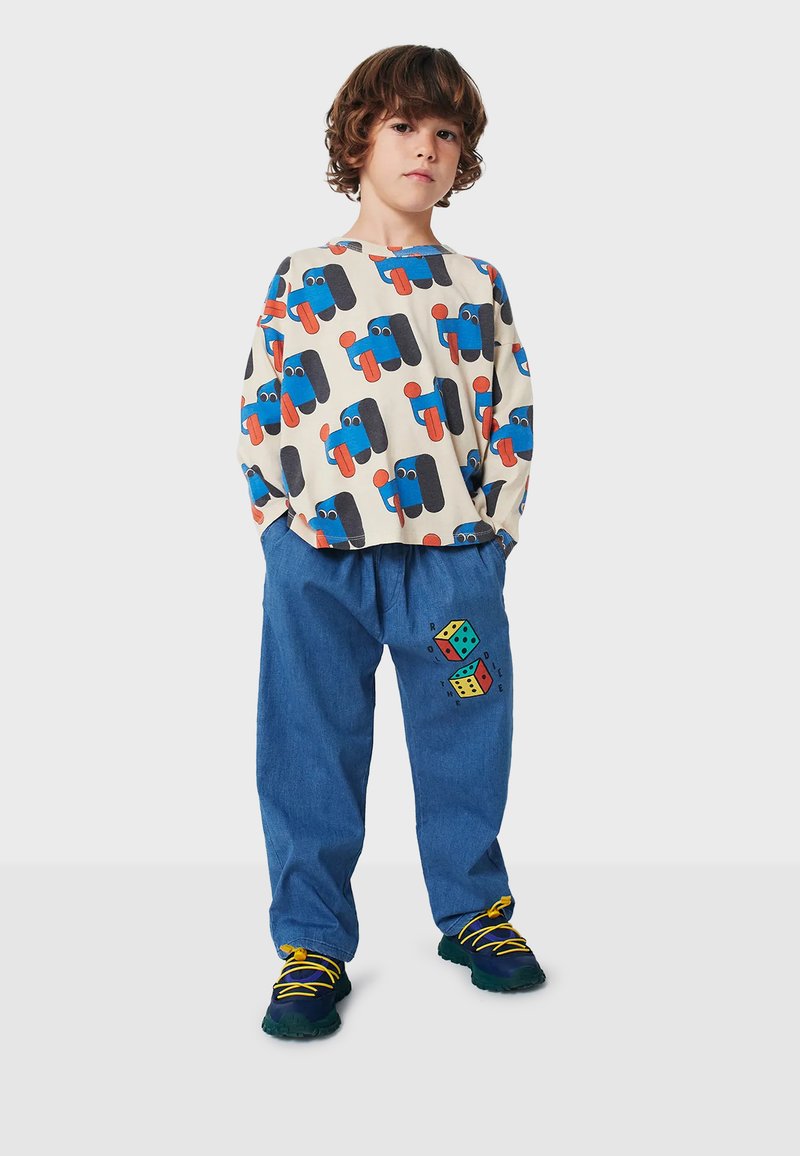 Camisa de manga larga color crema con un patrón de vehículos de dibujos animados en azul y naranja, combinada con pantalones azules que presentan un diseño de dados coloridos en una pierna.