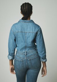 Jeanshemd und hochgeschnittene Jeans in Hellblau. Verfügt über einen Kragen, geknöpfte Manschetten und Gesäßtaschen mit sichtbarem Steppdetail.