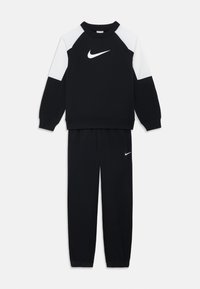 Felpa sportiva nera con accenti bianchi sulle spalle e logo Nike; abbinata a pantaloni della tuta neri con un piccolo logo Nike sulla coscia.
