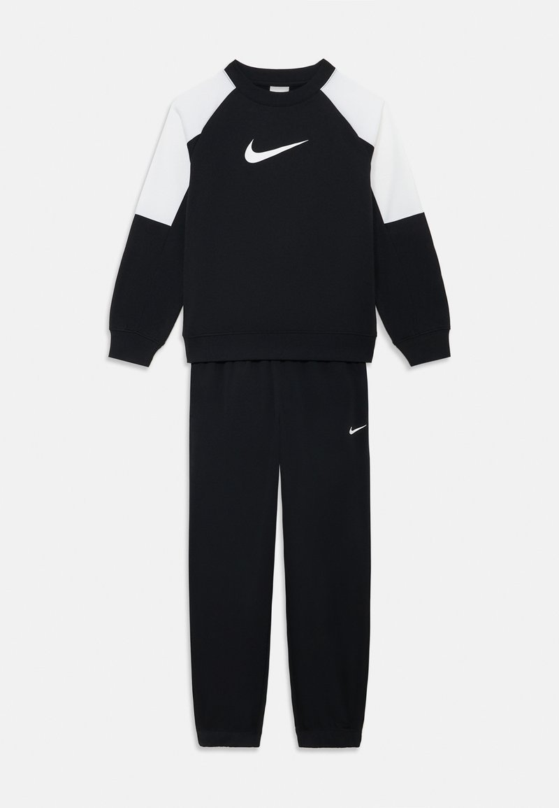 Felpa sportiva nera con accenti bianchi sulle spalle e logo Nike; abbinata a pantaloni della tuta neri con un piccolo logo Nike sulla coscia.