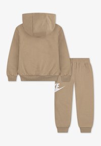Ensemble sweat à capuche beige et pantalon de jogging en tissu doux. Le sweat à capuche possède une poche kangourou à l'avant, des poignets élastiques, et les pantalons présentent un logo Nike blanc.