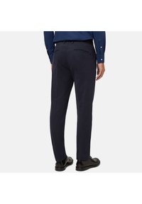 Temno modri hlače z gladko teksturo, ožji kroj in detajli žepov na hrbtni strani, v kombinaciji s črnimi čevlji, prikazane s hrbtne strani.