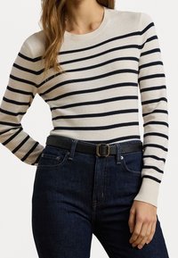 Béžový pletený svetr s tmavě modrými vodorovnými pruhy, kulatým výstřihem a dlouhými rukávy, doplněný tmavými džíny a černým opaskem se zlatou sponou.