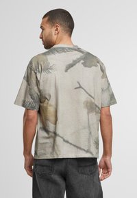 Kortermet, avslappet skjorte i beige med et naturinspirert trykk med blader og grener i dempede farger.