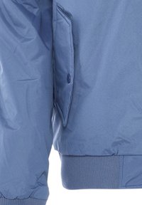 Šviesiai mėlynas pūkinis švarkas su mygtukais užsegama kišene ir raštuotais kraštais. Lygus, vandeniui atsparus audinys su šiek tiek blizgiu paviršiumi.