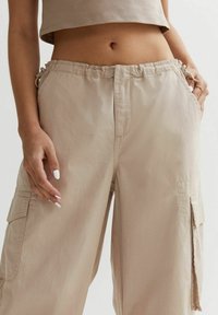 Béžové cargo kalhoty s elastickým pasem, bočními kapsami a hladkou texturou; lehká tkanina, s volným střihem a praktickým designem.