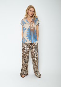 Beżowa koszulka krótki rękaw z niebieskim i brązowym abstrakcyjnym wzorem, zestawiona z szerokimi spodniami w panterkę, charakteryzującymi się luźnym krojem i casualowym stylem.