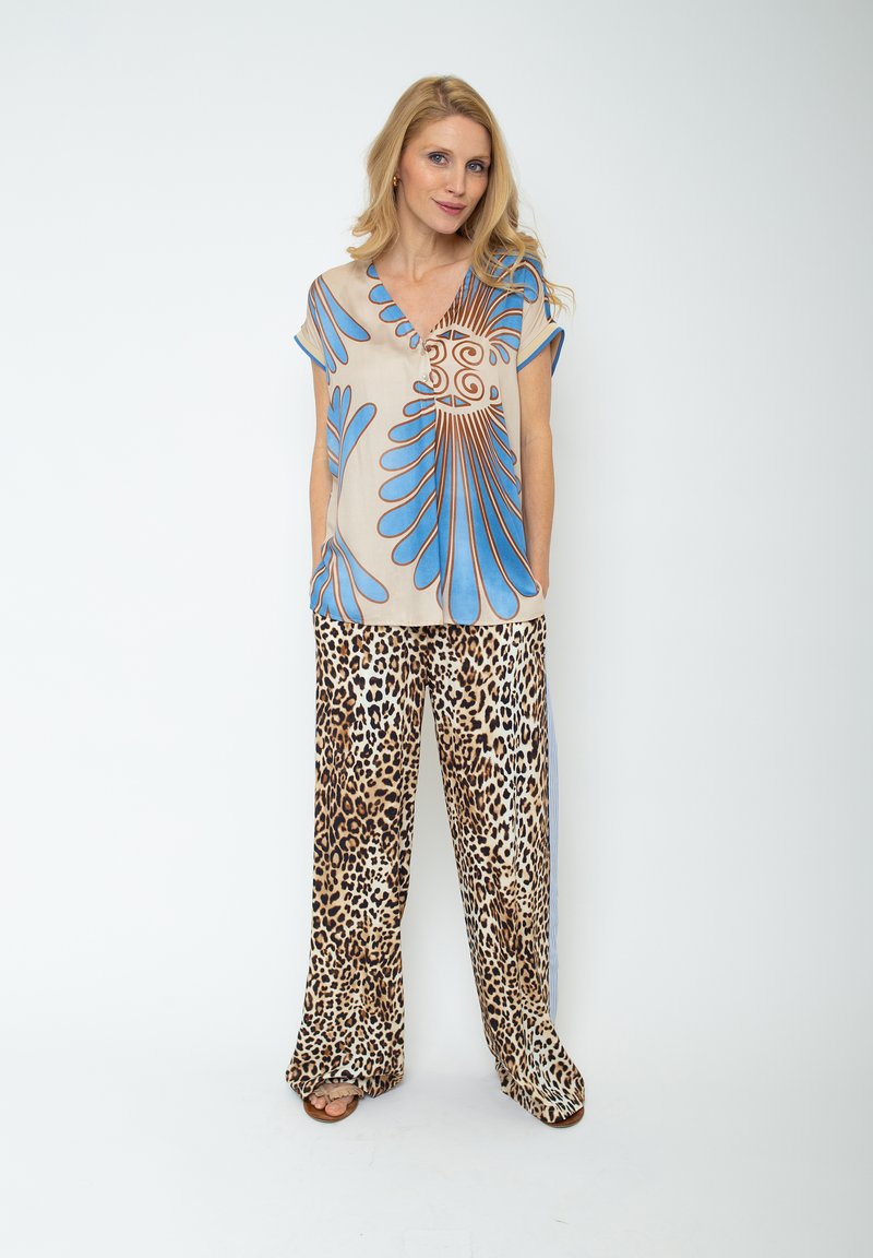 Beżowa koszulka krótki rękaw z niebieskim i brązowym abstrakcyjnym wzorem, zestawiona z szerokimi spodniami w panterkę, charakteryzującymi się luźnym krojem i casualowym stylem.