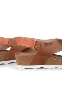 Sandali in pelle marrone con tacco in sughero, dotati di una fascia larga e fibbia regolabile. Sole in gomma bianca con finitura testurizzata.