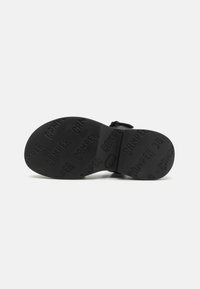 Svart gummisandal sula med texturerad yta där varumärket "CAMPER" är präglat upprepade gånger, rundad form, platt design.